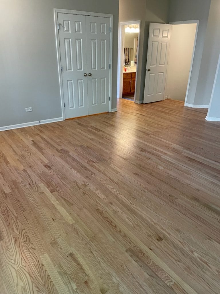 Natural oak hardwood flooring in a bedroom with white trim and closet doors, installed in New Lenox, IL by The Floor 4 U.