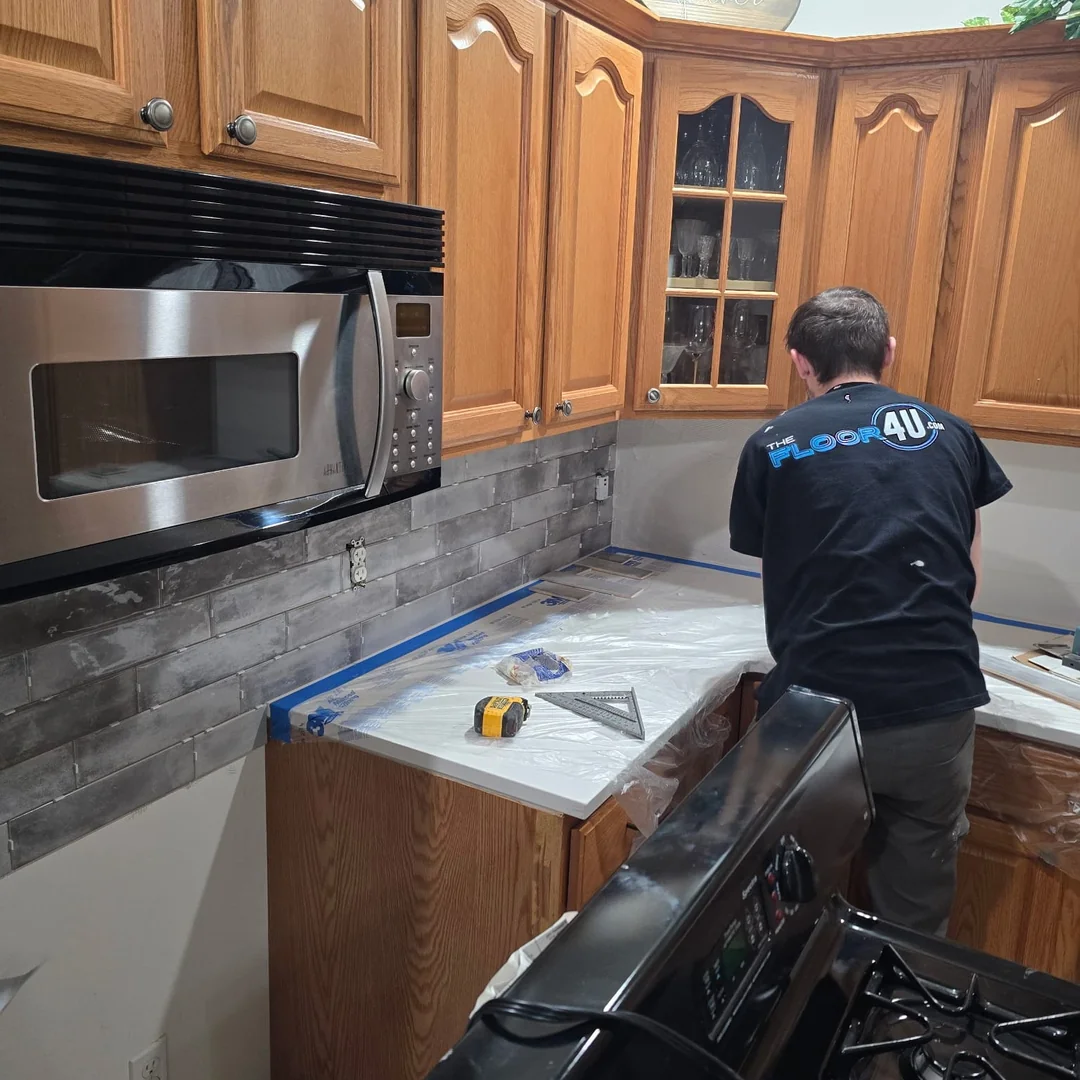The Floor 4U crew member in a branded shirt installing kitchen backsplash tile during a remodel